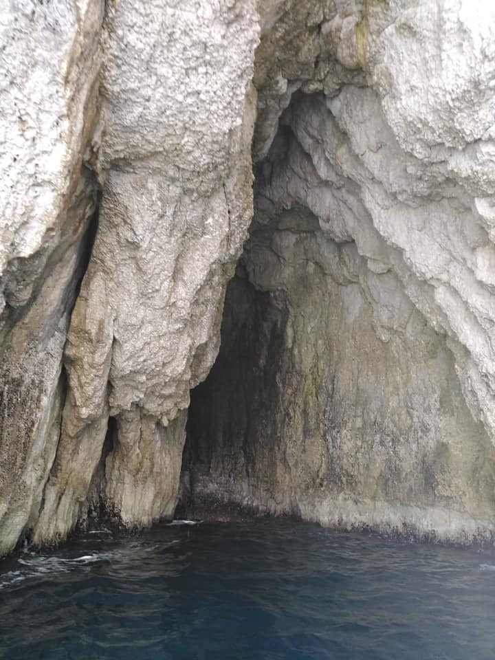 La fenditura nella roccia rivela una grotta accessibile con la barca. Il mare calmo permette alla barca di avvicinarsi